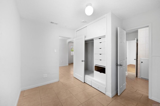 unfurnished bedroom featuring light tile patterned floors, arched walkways, a closet, and baseboards