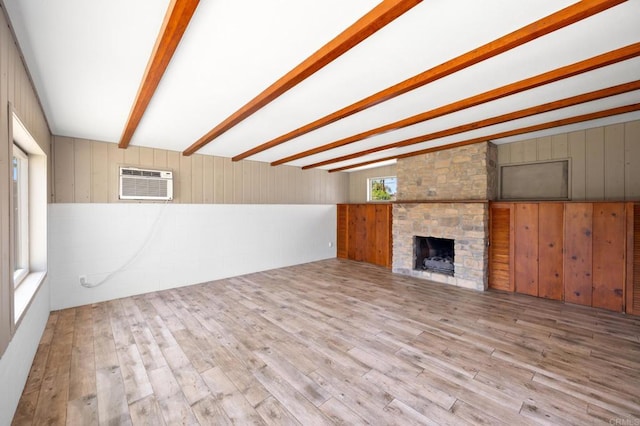 unfurnished living room featuring wood finished floors, wooden walls, beam ceiling, a wall unit AC, and a stone fireplace