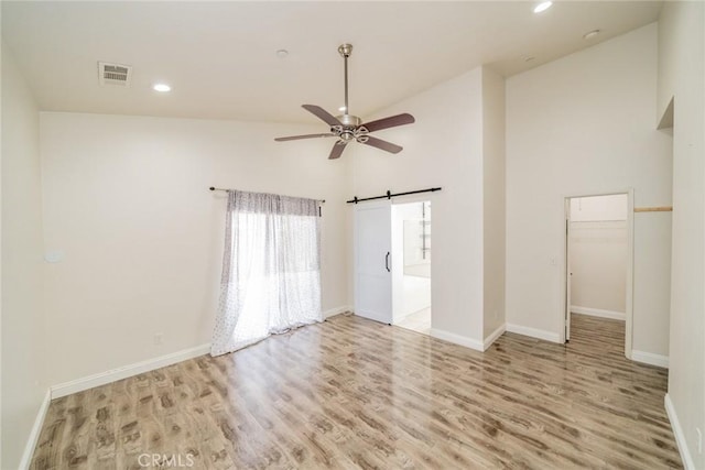 7404 Marshall Ct, Highland, CA 92346 - empty room with light wood-style flooring, ceiling fan, a barn door, high vaulted ceiling, and baseboards