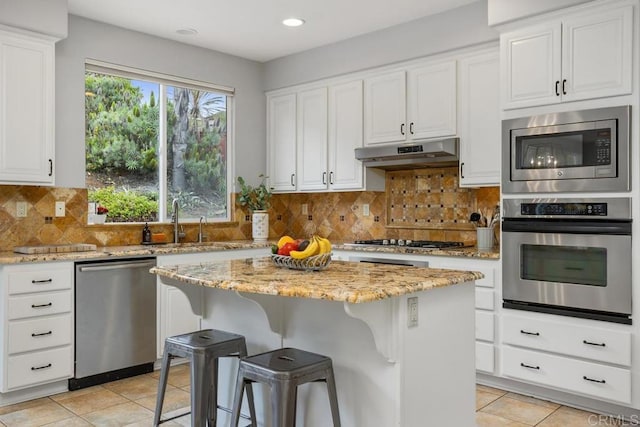 6628 Sitio Sago, Carlsbad, CA 92011 - kitchen featuring appliances with stainless steel finishes, under cabinet range hood, light tile patterned flooring, a sink, and white cabinets