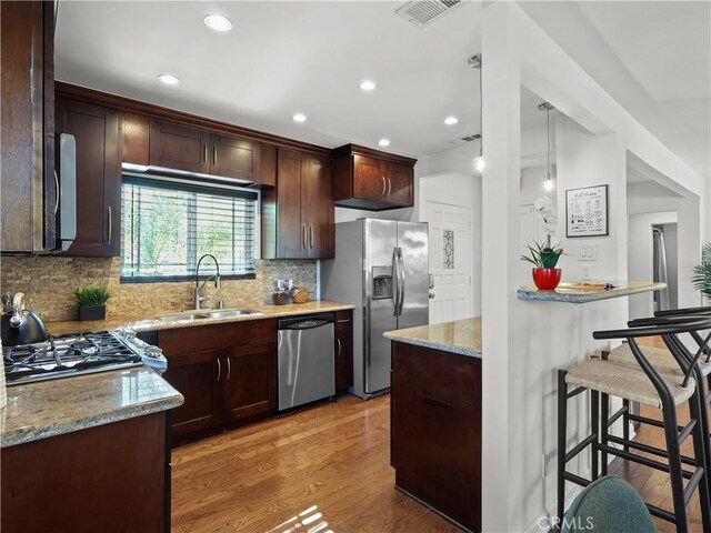 8110 Lesner Ave, Lake Balboa, CA 91406 - kitchen featuring stainless steel appliances, light stone countertops, a kitchen breakfast bar, tasteful backsplash, and light wood-style flooring