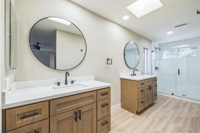 40550 Ventana Ct, Palm Desert, CA 92260 - bathroom with a textured wall, wood finished floors, a shower stall, two vanities, and a skylight