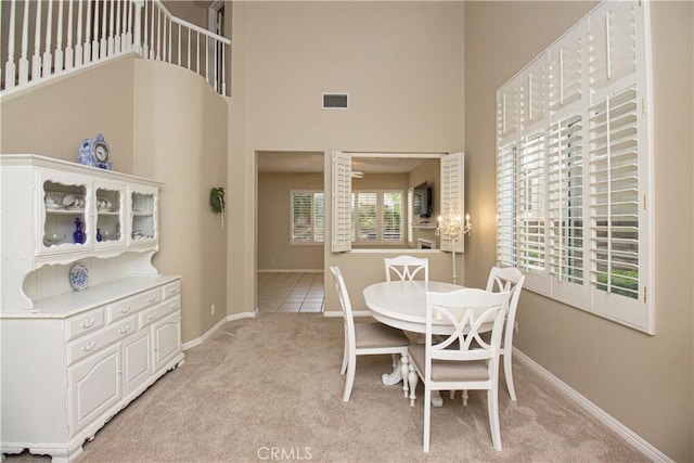 dining space with light colored carpet, a towering ceiling, and baseboards