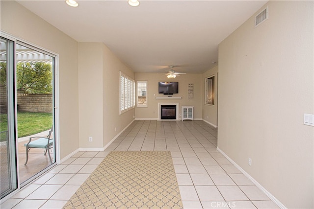 unfurnished living room with a glass covered fireplace, light tile patterned flooring, a ceiling fan, healthy amount of natural light, and recessed lighting