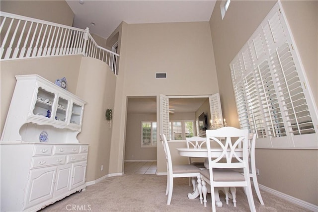 dining space with light colored carpet, a towering ceiling, and baseboards