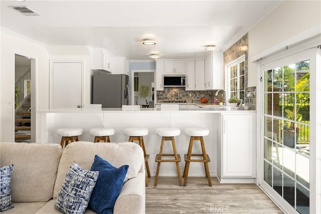 15541 Olive Branch Dr, La Mirada, CA 90638 - kitchen featuring appliances with stainless steel finishes, a kitchen breakfast bar, white cabinetry, backsplash, and light wood finished floors