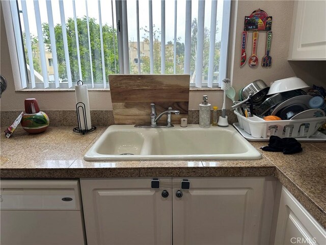 kitchen with white dishwasher, tile counters, a sink, and healthy amount of natural light