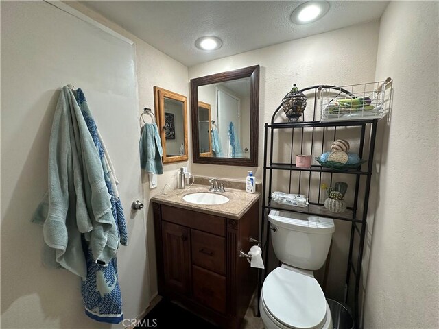 bathroom featuring vanity, toilet, a textured wall, and a textured ceiling