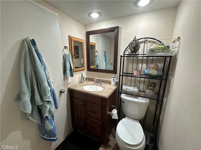 bathroom featuring toilet, vanity, and a textured wall