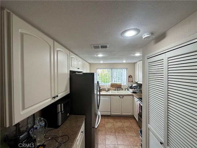 kitchen with white dishwasher, a sink, freestanding refrigerator, white cabinetry, and a textured ceiling