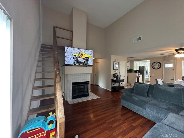living room with a ceiling fan, stairs, wood finished floors, high vaulted ceiling, and a tiled fireplace