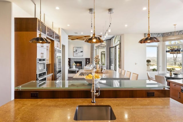 kitchen with a sink, stainless steel appliances, a lit fireplace, pendant lighting, and open floor plan