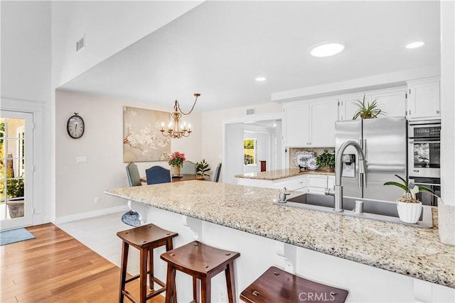 kitchen featuring appliances with stainless steel finishes, white cabinetry, baseboards, a peninsula, and a kitchen breakfast bar