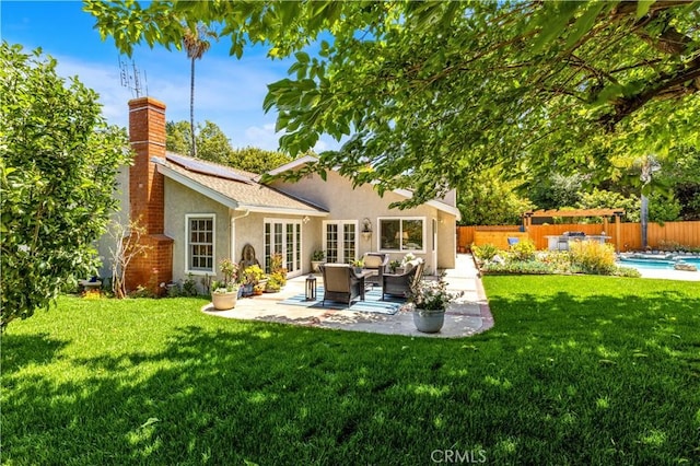 rear view of house with stucco siding, french doors, a chimney, a patio area, and roof mounted solar panels
