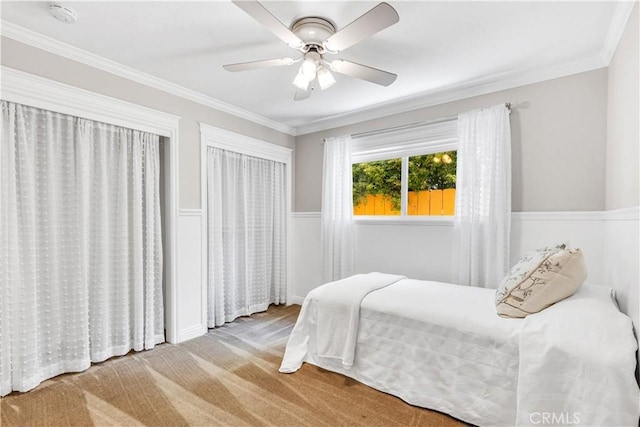 bedroom with carpet floors, a wainscoted wall, crown molding, and a ceiling fan
