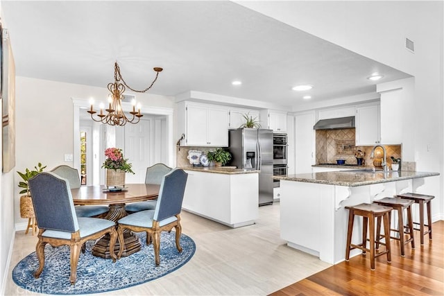 kitchen with appliances with stainless steel finishes, a peninsula, under cabinet range hood, a sink, and a chandelier