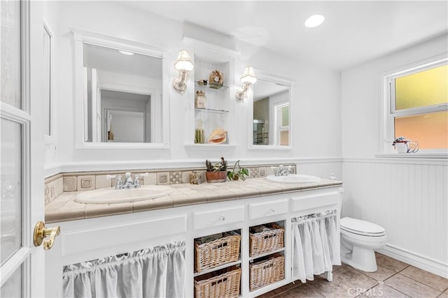 full bath featuring toilet, double vanity, plenty of natural light, and wainscoting