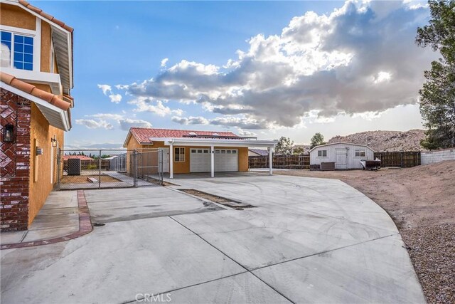 17725 Tude Ln, Apple Valley, CA 92307 - view of patio with concrete driveway, a gate, an attached garage, a carport, and an outdoor structure