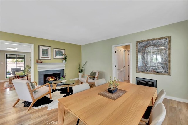 3235 Faust Ave, Long Beach, CA 90808 - dining room featuring a warm lit fireplace, baseboards, and light wood-style floors