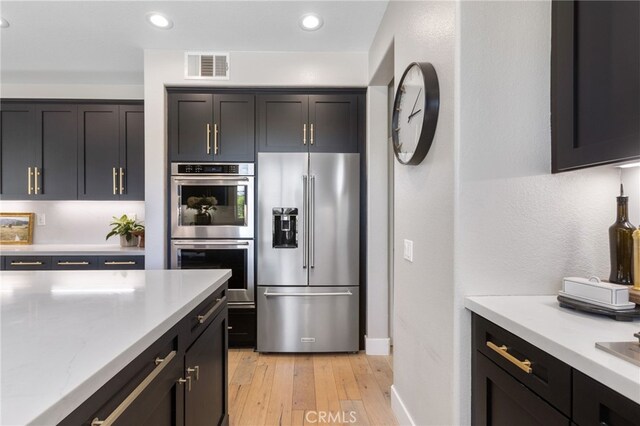 32429 Castle Ct, Temecula, CA 92592 - kitchen with appliances with stainless steel finishes, light wood-style flooring, baseboards, dark cabinets, and light stone countertops
