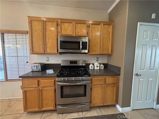1800 Windermere Dr, Lancaster, CA 93534 - kitchen featuring appliances with stainless steel finishes, dark countertops, light tile patterned floors, brown cabinets, and ornamental molding