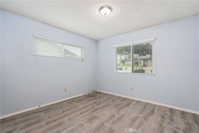 unfurnished room featuring a textured ceiling, wood finished floors, and baseboards