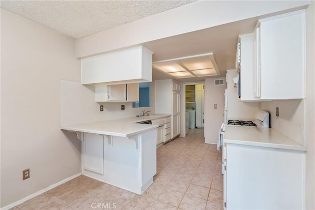kitchen featuring a breakfast bar area, a peninsula, light countertops, white cabinets, and washer / dryer