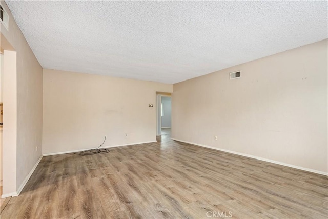empty room with light wood-style floors, a textured ceiling, and baseboards