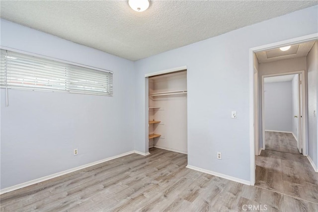 unfurnished bedroom featuring wood finished floors, a closet, attic access, a textured ceiling, and baseboards