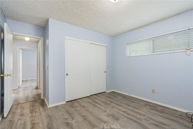 unfurnished bedroom with wood finished floors, a closet, baseboards, and a textured ceiling