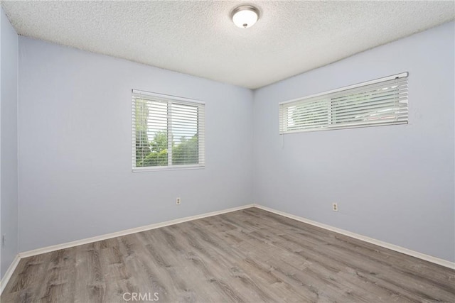unfurnished room with a textured ceiling, wood finished floors, and baseboards