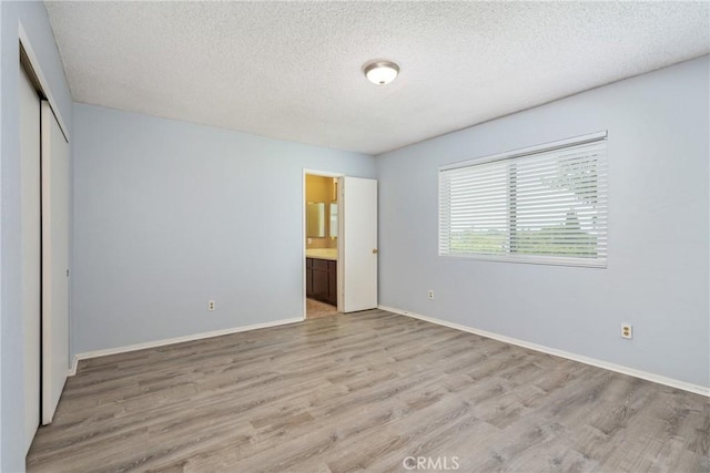 unfurnished bedroom with light wood finished floors, a textured ceiling, a closet, baseboards, and ensuite bath
