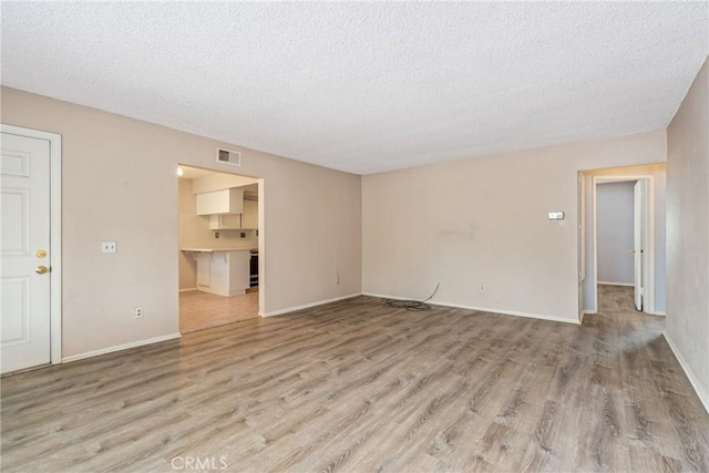 unfurnished room with a textured ceiling, light wood-style flooring, and baseboards
