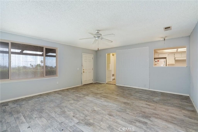 unfurnished room with a textured ceiling, ceiling fan, wood finished floors, and baseboards