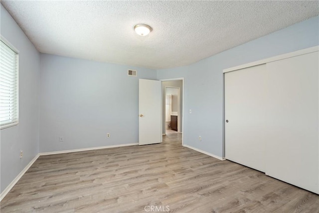 unfurnished bedroom featuring a textured ceiling, wood finished floors, a closet, and baseboards