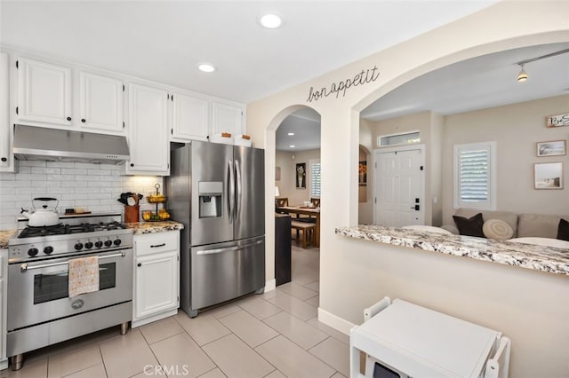 130 Bloomfield Ln, Rancho Santa Margarita, CA 92688 - kitchen featuring under cabinet range hood, stainless steel appliances, backsplash, arched walkways, and light stone counters