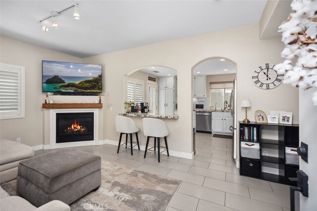 130 Bloomfield Ln, Rancho Santa Margarita, CA 92688 - living room with light tile patterned flooring, rail lighting, arched walkways, a glass covered fireplace, and baseboards