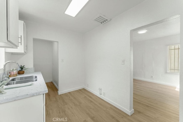9309 S Broadway, Los Angeles, CA 90003 - kitchen featuring a sink, light wood-type flooring, white cabinetry, and baseboards