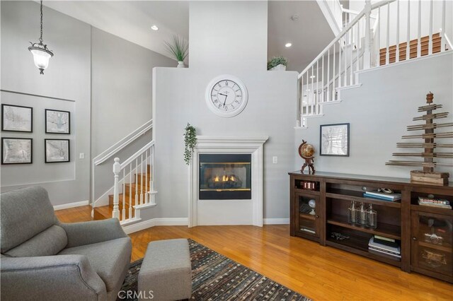 23423 Waterway Ln Unit 17, Valencia, CA 91355 - living room featuring a high ceiling, stairway, wood finished floors, a glass covered fireplace, and baseboards