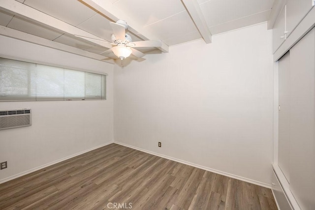 unfurnished room featuring beam ceiling, wood finished floors, a ceiling fan, baseboards, and a wall unit AC