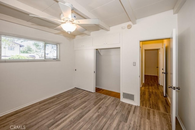 unfurnished bedroom with wood finished floors, beam ceiling, a closet, and baseboards