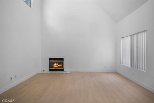 14937 Dickens St Unit 209, Sherman Oaks, CA 91403 - unfurnished living room with high vaulted ceiling, light wood-style flooring, a fireplace with flush hearth, and baseboards
