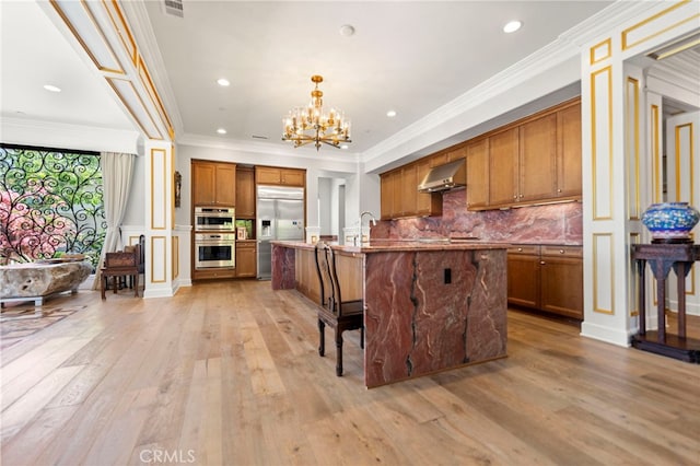 2825 Majestic St, West Covina, CA 91791 - kitchen with appliances with stainless steel finishes, brown cabinets, wall chimney exhaust hood, light wood-style flooring, and a chandelier