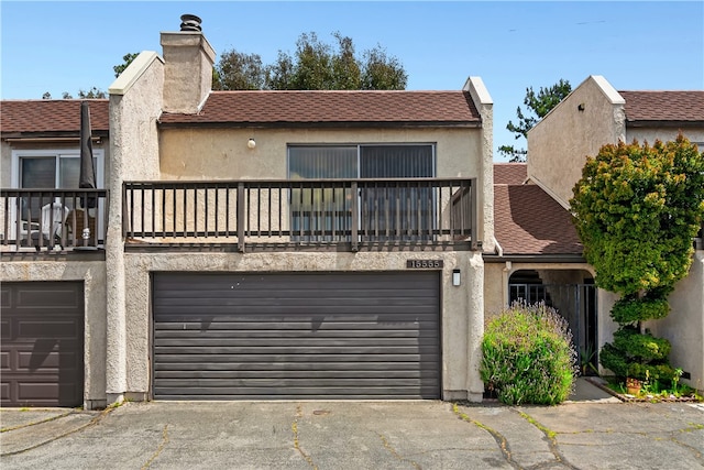 view of front of house featuring a balcony, a garage, a chimney, stucco siding, and driveway