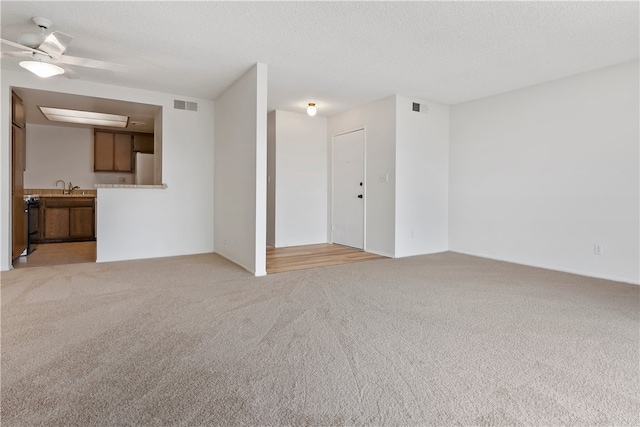 unfurnished living room featuring light colored carpet, a ceiling fan, a textured ceiling, and a sink