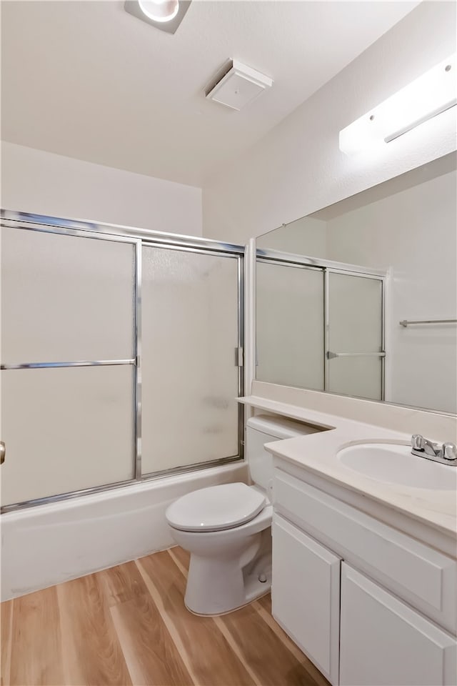 full bathroom with wood finished floors, toilet, vanity, and combined bath / shower with glass door