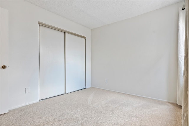 unfurnished bedroom with carpet, a closet, a textured ceiling, and baseboards