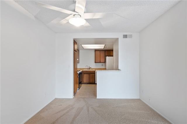 unfurnished living room with light carpet, a ceiling fan, a textured ceiling, and a sink
