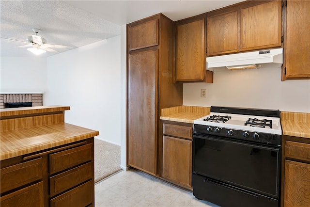 kitchen featuring gas range oven, under cabinet range hood, ceiling fan, light countertops, and a textured ceiling