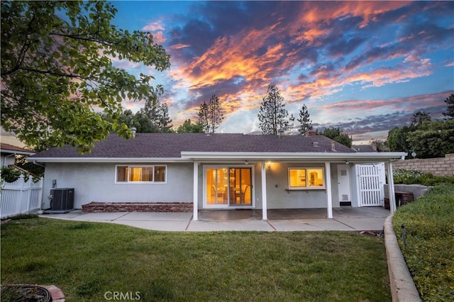 back of house at dusk featuring stucco siding, a patio area, roof with shingles, and central air condition unit
